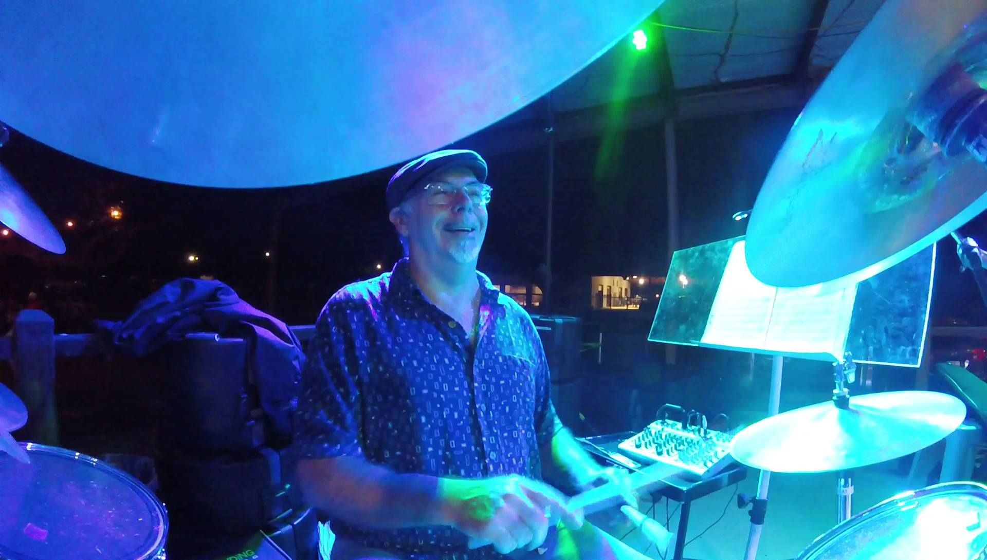 Bruce Wayne drumming on stage under blue and green lights
