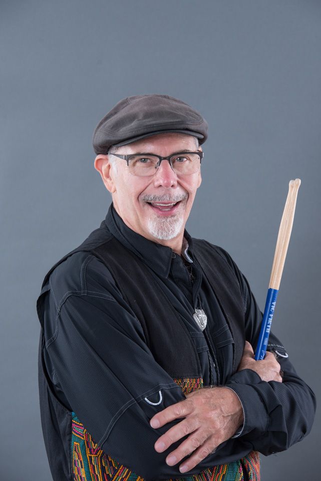 Bruce Wayne with a pair of drumsticks, arms folded