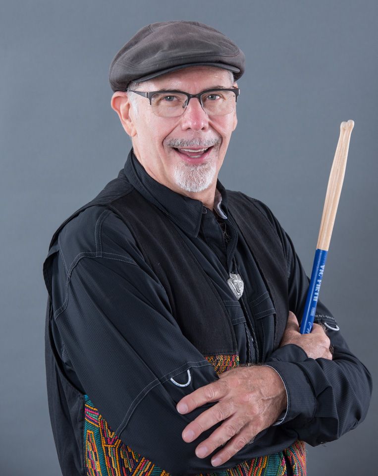 Bruce Wayne in a flat cap, holding a drumstick